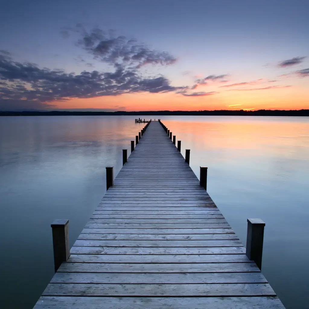 Wooden dock leading out to lake at sunset