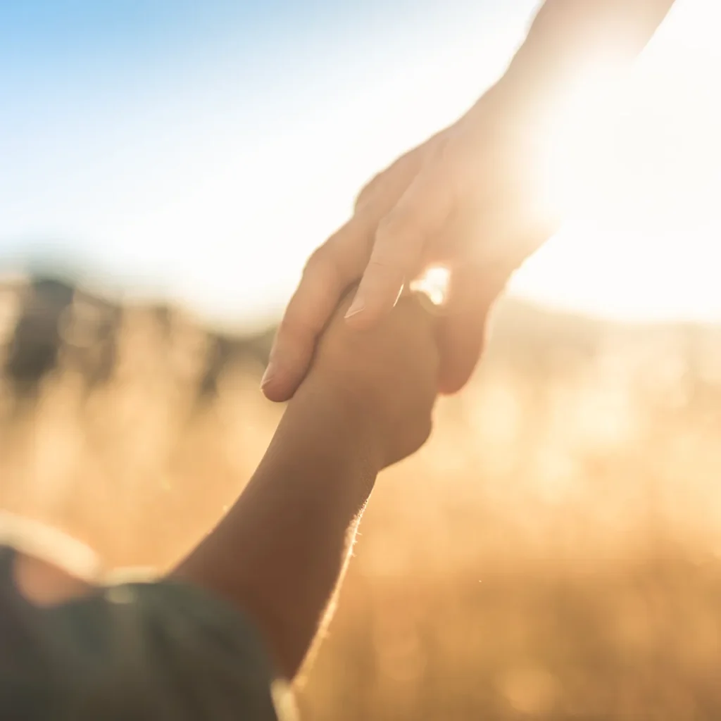 Adult and child holding hands with bright sunlight in background